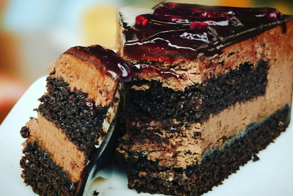 Decadent dessert featuring a rich chocolate cake layered with creamy, chocolate mousse and topped with a glossy cherry sauce.