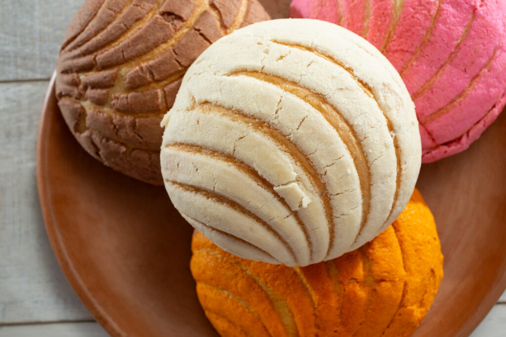 Dessert shells recipes: A selection of colorful conchas, traditional Mexican sweet bread, on a wooden plate.